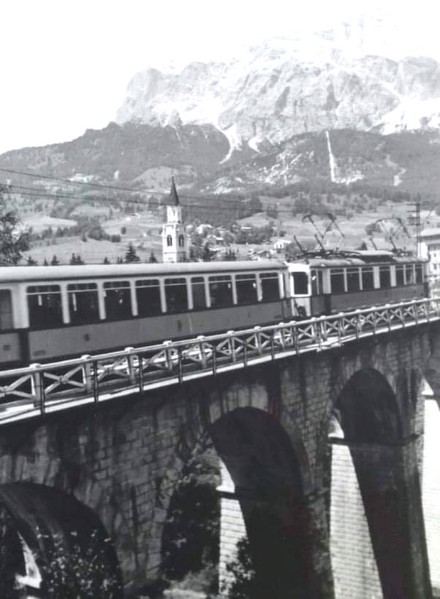 26b) Maggio 1961, il treno della Ferrovia Dolomiti Calalzo Cortina passa sul ponte Bigontina ed entra in Stazione in perfetto orario. Sullo sfondo la Cortina degli anni sessanta..jpg