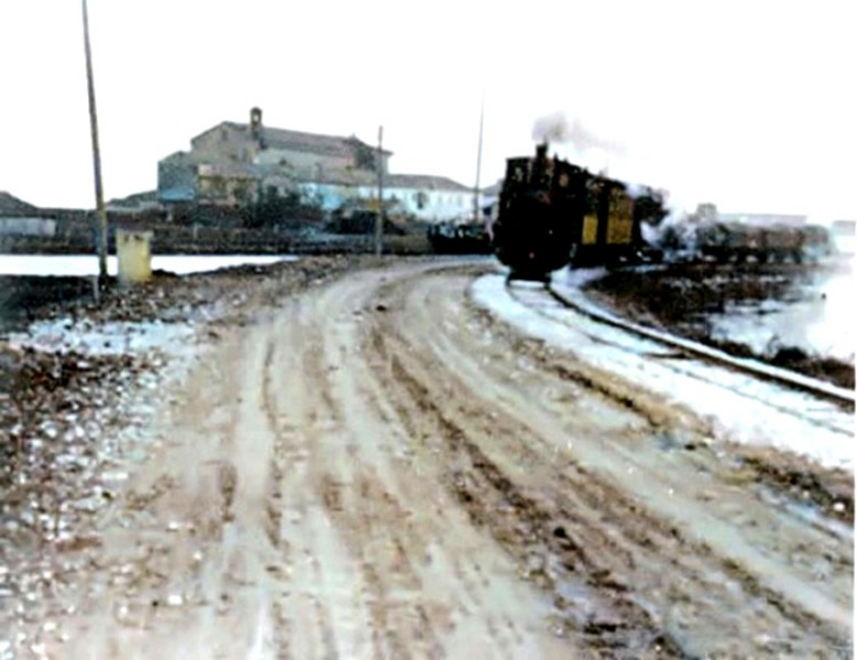 138) Comacchio (Cappuccini), il treno proviene da Ostellato e corre sulla strada argineSpina; la chiesa dei Cappuccini è alle spalle del treno; a sx il canale provinciale.jpg